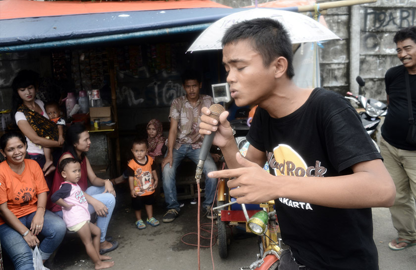 A member of the public entertaining revellers as he sings from the karaoke machine attached to Rudi Hantoro's pedal-powered rickshaw on March 15, 2016 in Depok. - AFP Photo