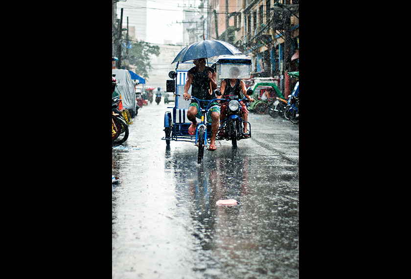 A tricycle driver and pedicab seen driving through the rain in Quiapo, Manila. - Photo by Karim Raslan