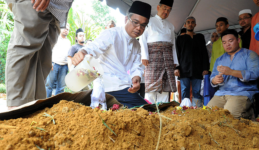 Abdul Aziz's youngest son, Imanuddin, pouring rose water over his father's grave at the Kampung Rim Muslim Cemetery in Jasin, Malacca on Oct 4, 2016. - BERNAMApic