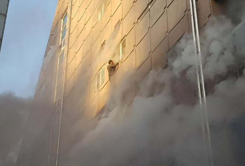 A survivor dangles from a windowsill as he waits for rescue from the burning building on Dec 21, 2017. - REUTERS