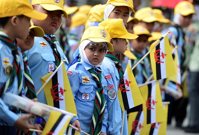 Aksi meriah kumpulan kanak-kanak dengan pakaian seragam yang turut meraikan upacara perarakan Sultan Brunei di jalanan. - Reuters