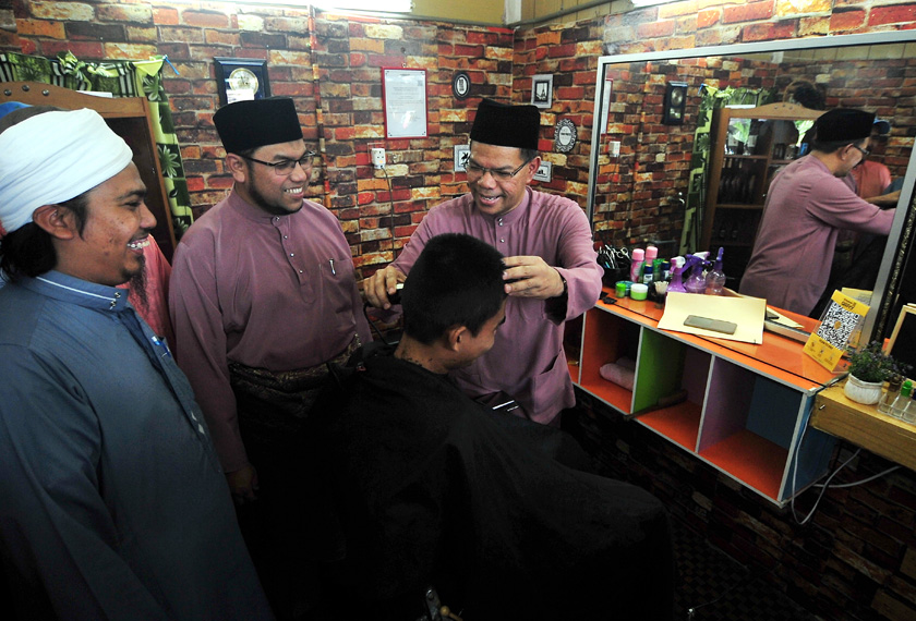 Saifuddin menunjukkan bakat menggunting rambut salah seorang pelanggan ketika bertemu Pengusaha Kedai Gunting Rambut Shady Saiful Shamsudin (kiri), yang merupakan penerima Bantuan Peralatan Ekonomi Usahawan Daerah Barat Daya hari ini. - BERNAMA