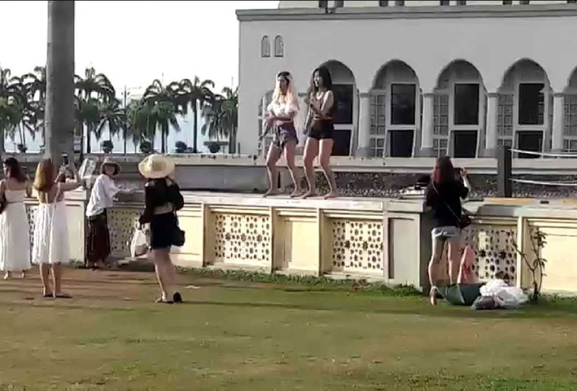 Kelihatan dua pelancong asing naik di atas pagar Masjid Bandaraya Kota Kinabalu dan menari aksi seksi.