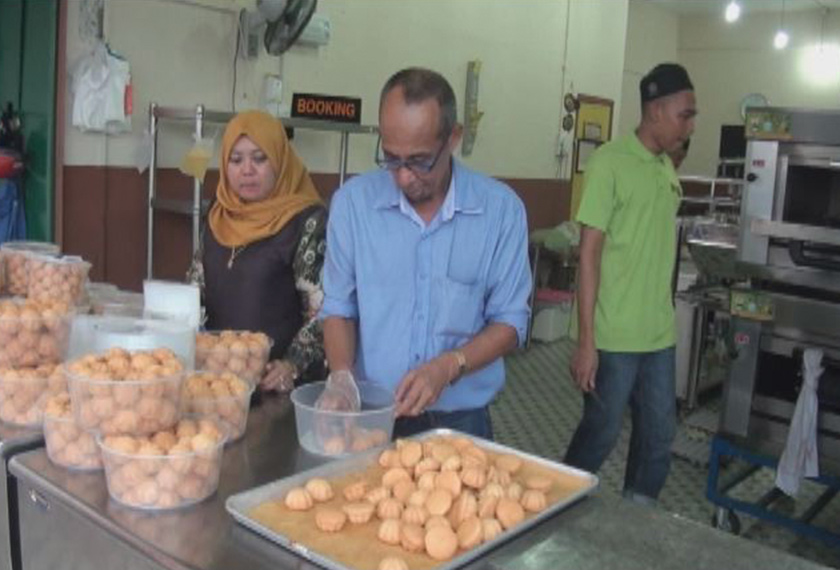 Pak Din (kiri) sibuk mengisi kuih bahulu panas ke dalam bekas sebelum diedarkan kepada pembeli.