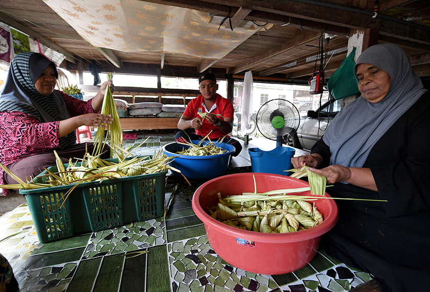 Zainab dibantu dua anaknya Mohd Azwan Ismail, 30, (tengah) dan Nor Aida, 41, (kiri) menyediakan ketupat palas yang ditempah oleh pelanggan ketika ditemui di Kampung Bukit Tunggal, pada Jumaat. - BERNAMA