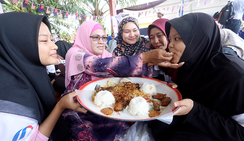 Ibu angkat kepada pewaris muda Faridah Mahmud, 61, (dua, kiri) menyuapkan makanan tradisional masyarakat jawa iaitu nasi ambeng kepada anak angkatnya Mira Haris Hasim,19, (kanan) pada Program penutup Pewaris Muda Peringkat Kebangsaan 2018 Jabatan Penerangan Malaysia di Kampung Parit Bugis pada Sabtu. - Bernama