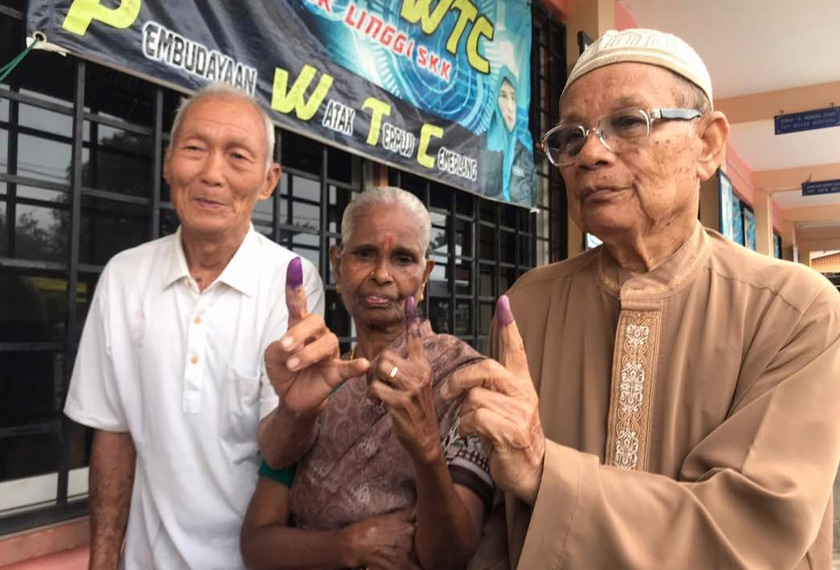 Abdul Aziz (kanan) dan dua orang pengundi lagi menunjukkan jari yang telah dicelup dakwat selepas membuang undi di SK Linggi hari ini. - Astro AWANI / SHUHADA KADIR