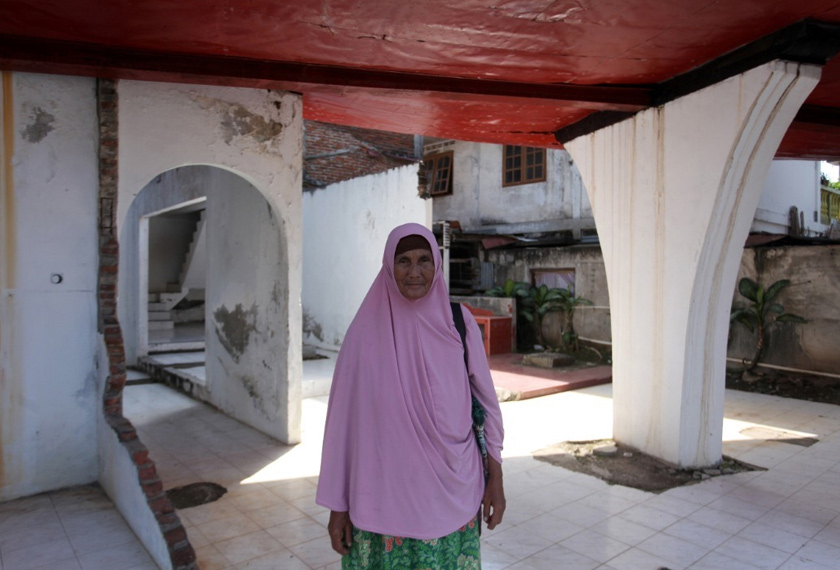 Mundiyah Sahan berdiri di bawah sebuah bot besar yang dihanyut arus dan hingga kini tersadai di atas sebuah bangunan. - Reuters