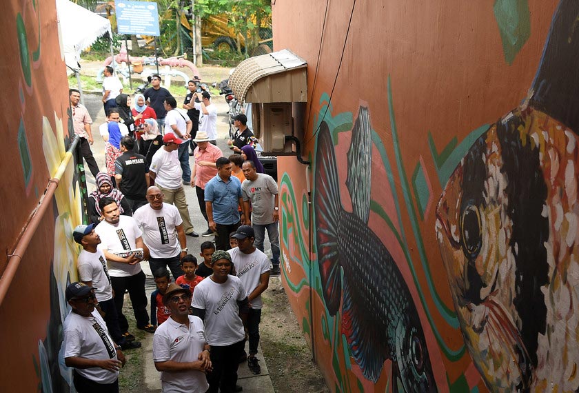 Muhammad Bakhtiar (bertopi) memerhatikan mural yang dihasilkan pada dinding Flat Lily semasa melawat mural-mural yang dihasilkan oleh pelukis tempatan di kawasan Balik Pulau. - Bernama