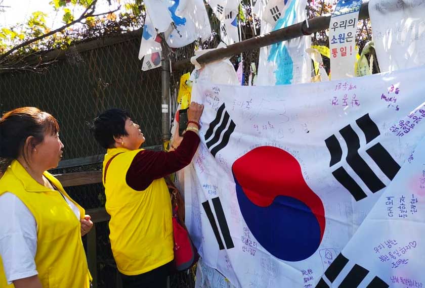 Pengunjung menulis harapan mereka pada bendera yang digantung pada pagar di hujung Freedom Bridge. - Astro AWANI