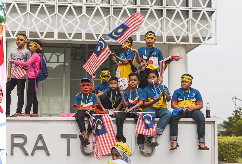 Sekumpulan kanak-kanak lelaki duduk di tepi tembok sambil menyaksikan perarakan sempena sambutan Hari Merdeka di Putrajaya. Pasukan Ceritalah