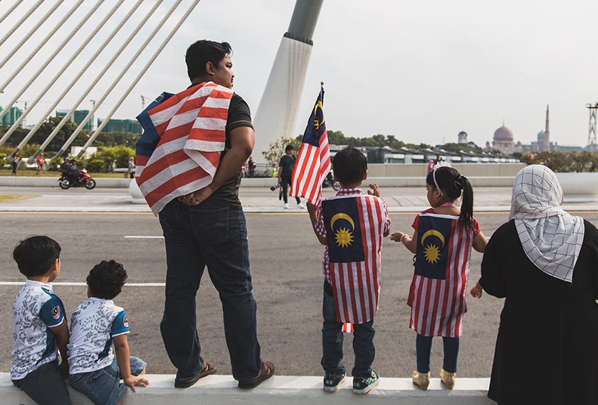 Seorang lelaki bersama dua anaknya memakai pakaian Jalur Gemilang menunggu bermulanya perarakan sempena sambutan Hari Merdeka di Putrajaya. Pasukan Ceritalah