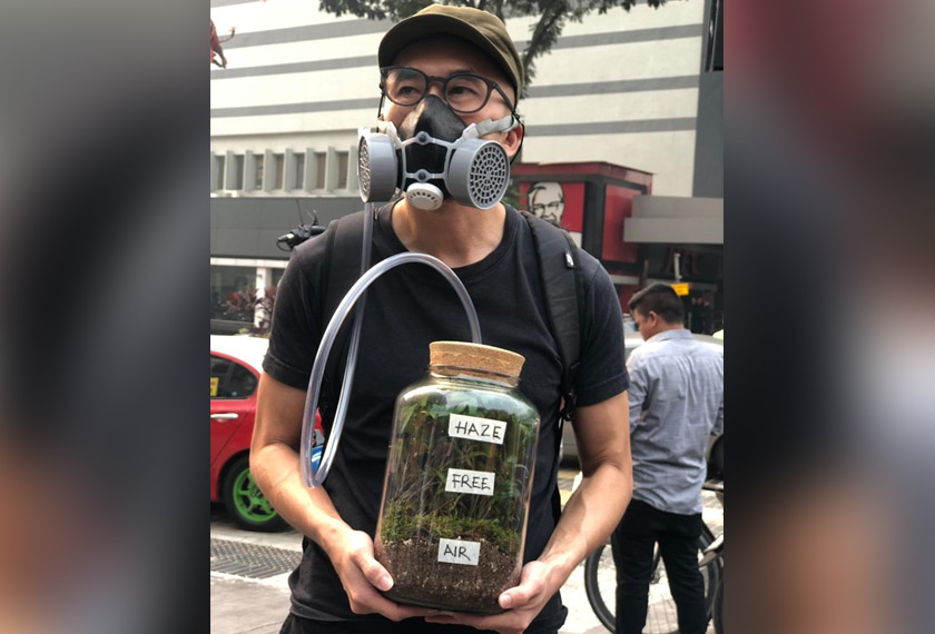 Salah seorang peserta memakai topeng muka dengan membawa balang tumbuhan sebagai simbolik jerebu yang dihadapi rakyat ketika ini