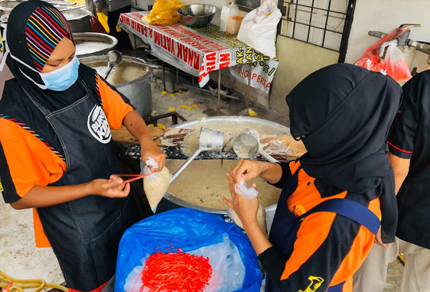 Pekerja Pak Zainal membungkus bubur lambuk yang siap dimasak sebelum dijual atau diambil oleh mereka yang telah menempahnya. - Foto Astro AWANI