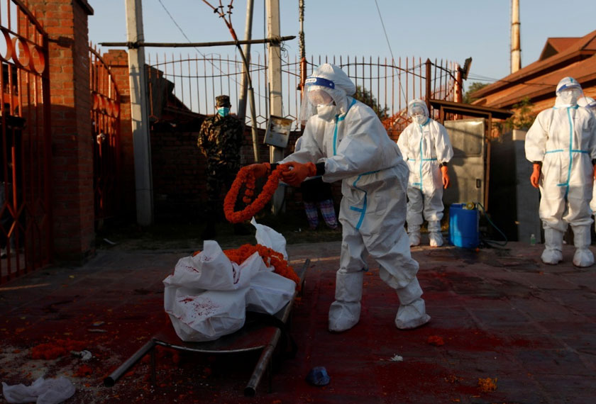 A female soldier wearing personal protective equipment (PPE) offers a garland on the body of a coronavirus victim provided by the family members at the crematorium. REUTERSpic