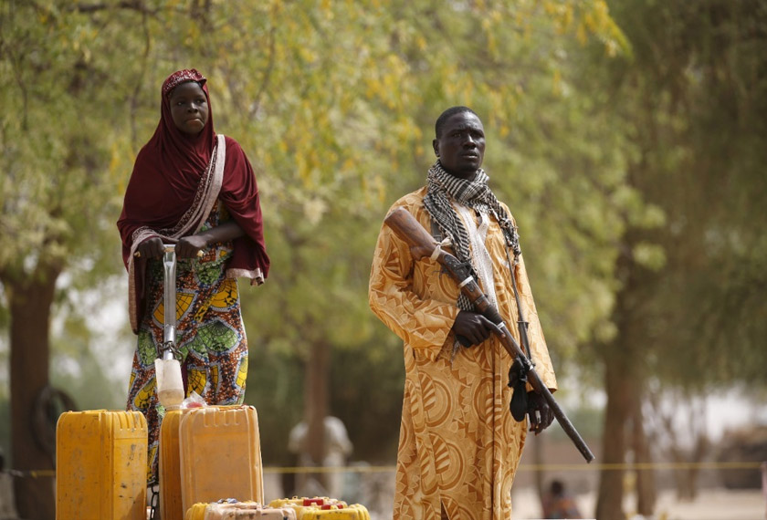 A member of a civilian vigilante group holds a hunting rifle while a woman pumps water into jerrycans in Kerawa, Cameroon. REUTERS file pic