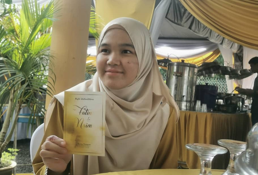 Adik bakal pengantin perempuan, Farah Dinie Ismail menunjukkan kad undangan majlis perkahwinan kakaknya, Fatin Nabilah Huda Ismail dengan Naim Hariri Kamaruddin. – Gambar Astro AWANI