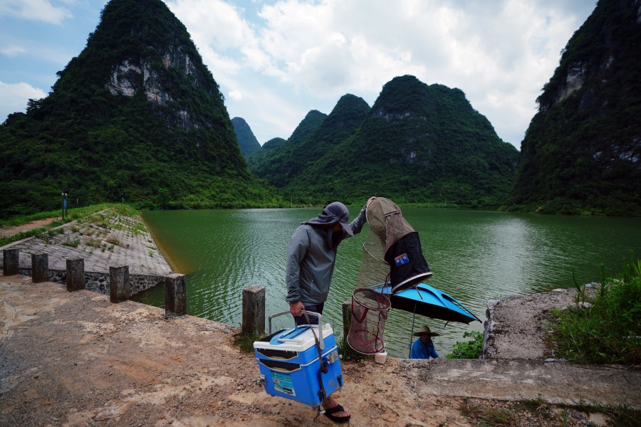 A man walks past the Longcheng reservoir with fishing equipment in Yangshuo county, Guangxi Zhuang Autonomous Region, China July 16, 2020 - REUTERS/Thomas Suen