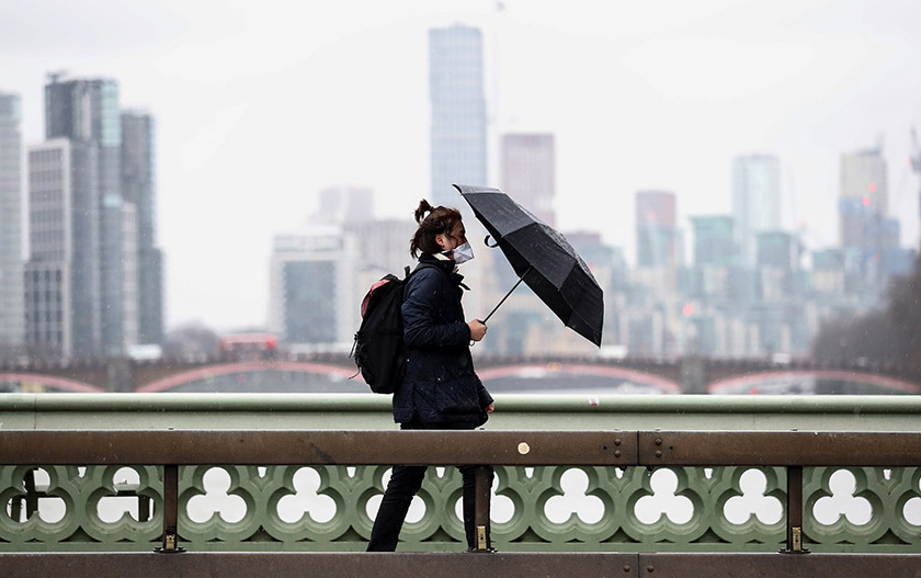 Seorang lelaki yang memakai penutup muka dan hidup berjalan di Jambatan Westminster di London, Britain, pada 5 Mac, 2020. - REUTERS