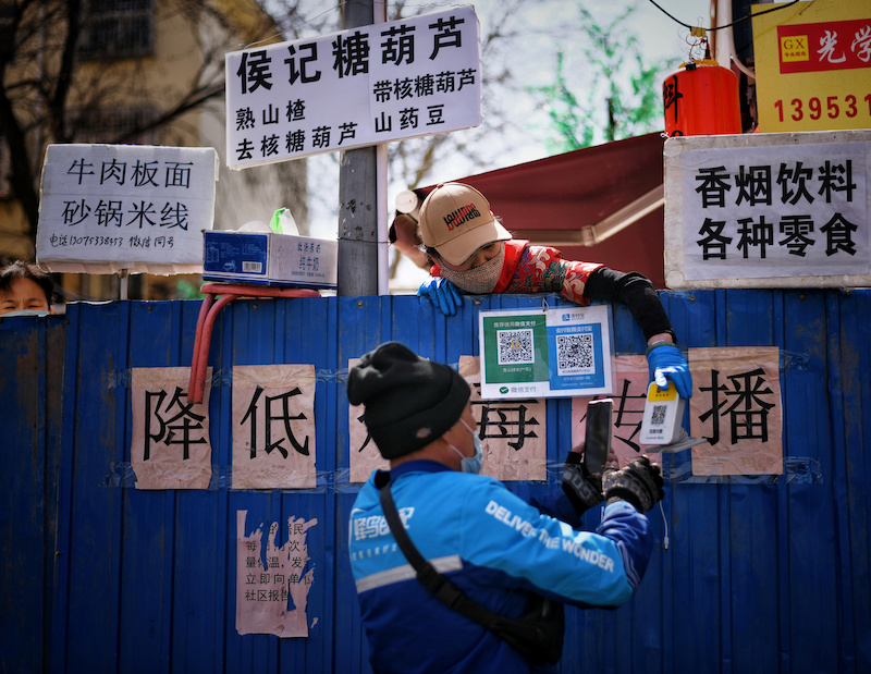 A deliveryman scans a QR code from an employee of a restaurant as he picks up food over barriers which has been set up to block an entrance to a food street, following an outbreak of the novel coronavirus in the country, in Jinan, Shandong province, China March 15, 2020. Picture taken March 15, 2020. China Daily via REUTERS