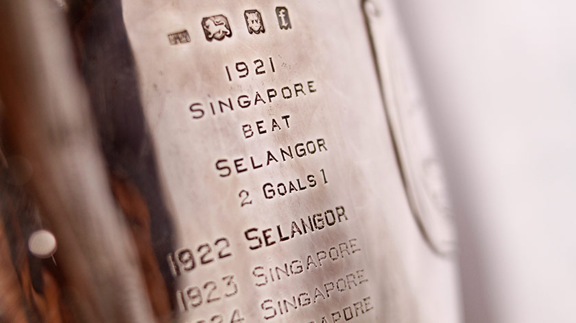 Ukiran di atas Piala HMS bola sepak memaparkan Singapura pasukan pertama menjulang piala berkenaan pada tahun 1921.