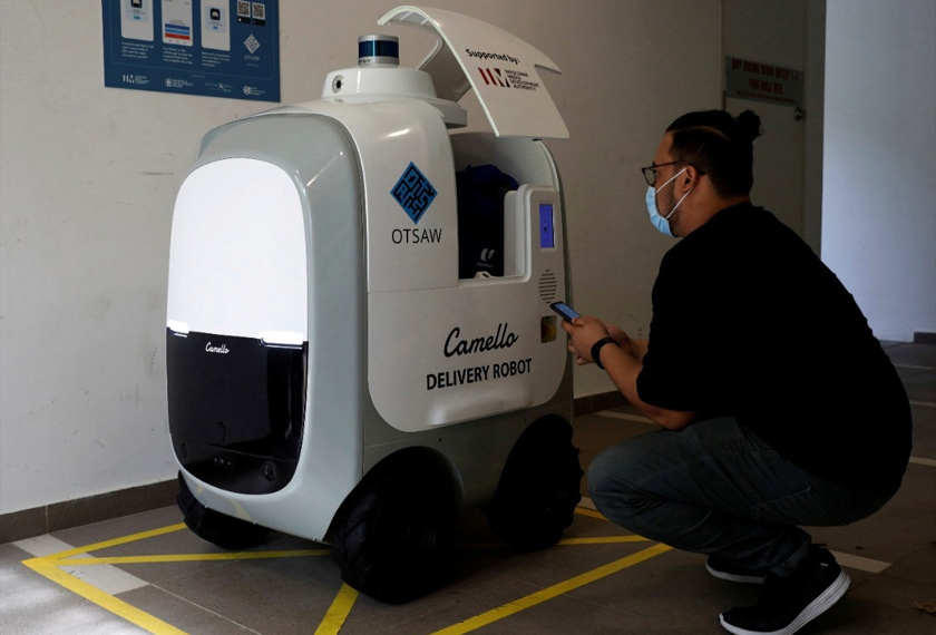 A customer collects his groceries from Camello, an autonomous grocery delivery robot, in Singapore. - REUTERS