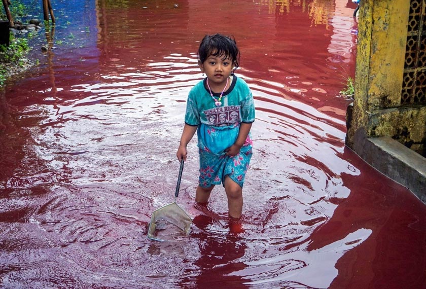 Seorang kanak-kanak leka mengharung air banjir merah di kawasan rumahnya. - Reuters