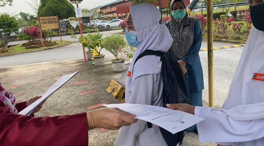 Guru menyerahkan borang deklarasi saringan COVID-19 kepada calon SPM.