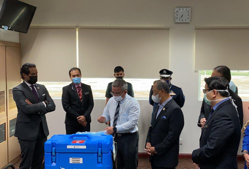 Datuk Seri Dr Adham Baba menunjukkan penggunaan picagari ‘low dead volume’ kepada Tan Sri Muhyiddin Yassin di Pusat Pemberian Vaksin (PPV) di Institut Kanser Negara pada petang Isnin. -  Gambar Astro AWANI