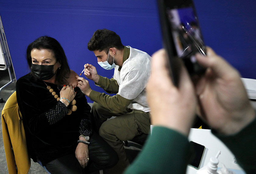 A woman receives a vaccination against the coronavirus disease (COVID-19) at a temporary healthcare maintenance organisation (HMO) centre, as a friend photographs her, amid Israel's third national lockdown, at an underground parking lot in Givatayim Mall, near Tel Aviv, Israel January 19, 2021. REUTERS/Ammar Awad