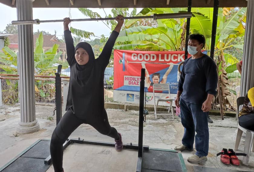   Ahmad Janius memantau teknik seorang bakat muda tempatan dalam sukan angkat berat di garajnya, di Kampung Kesang Tua, Jasin. - Astro AWANI 