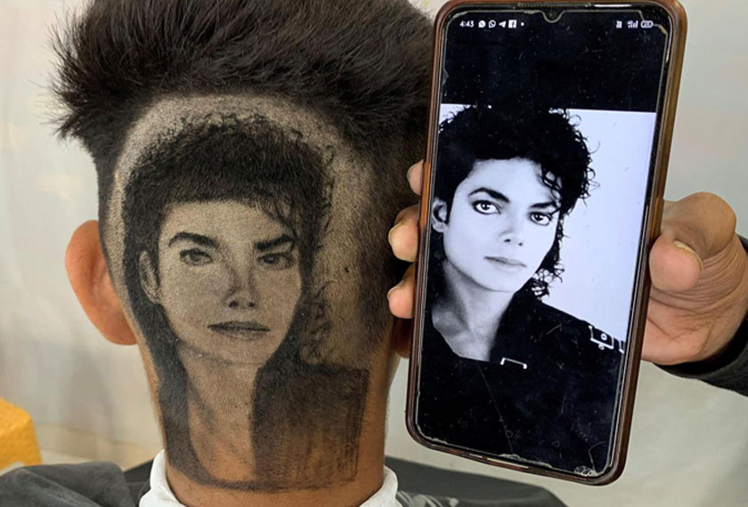 Gurwinder Singh displays a photo of Michael Jackson next to a customer after he made a hair tattoo of the pop star in the customer's hair inside his shop in Dabwali town, in the northern state of Punjab, India. - REUTERS