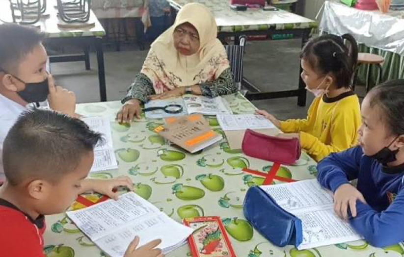 Saadiah (tengah) menggunakan kerusi roda mendidik murid di SK Masai.