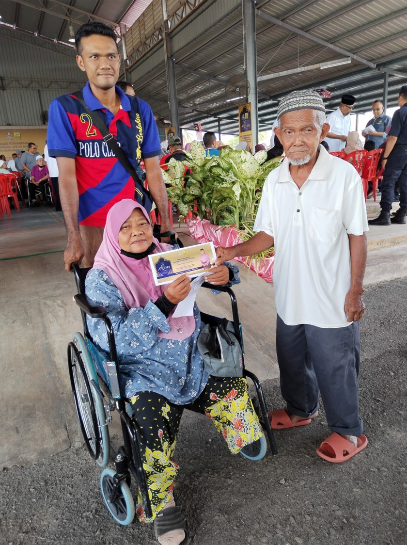 Zaini Mahmood (atas kerusi roda)  bersama keluarga sempena Majlis Penyampaian Sumbangan  Ahlan Ramadan Yayasan Pahang 2023 di Dewan Terbuka Laman Sejahtera Jelai, Felda Koyan 1 di sini pada Sabtu. - Foto Astro AWANI