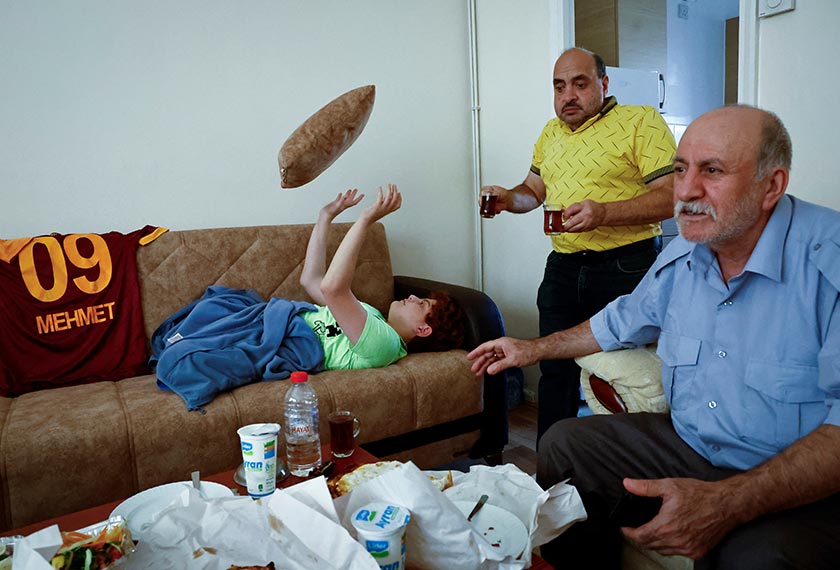 Hasan Koc, 58, brings tea for his son Mehmet, 13, and friend Ali Cinar, 63, at his apartment in London, Britain. - REUTERS