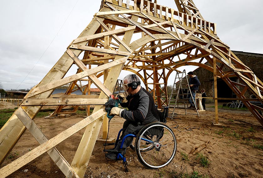 French carpenter Frederic Malmezac and Sylvain Bouchard, a sports enthusiast with disability, work on a 16-meter replica of the Eiffel Tower built from recycled wood. - REUTERS