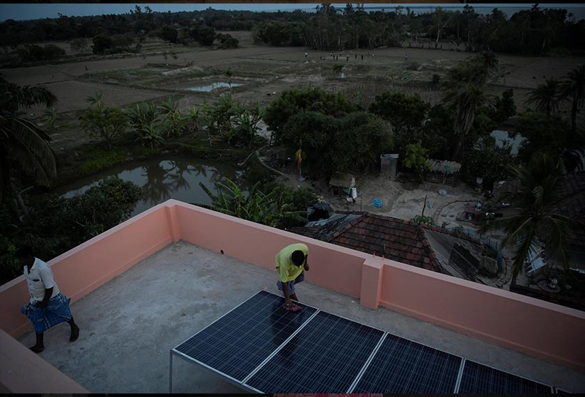 Debasish Paul, 62, a volunteer who works independently on environmental awareness and protection of the island, cleans solar panels on top of a flood shelter on Ghoramara Island in the Sundarbans, West Bengal, India. - REUTERS