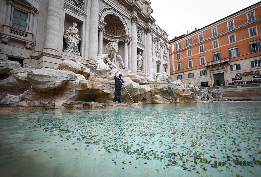 Daniele Rapiti, a worker at the ACEA utility company, uses a broom to gather coins to be collected at the Trevi Fountain in Rome, Italy,