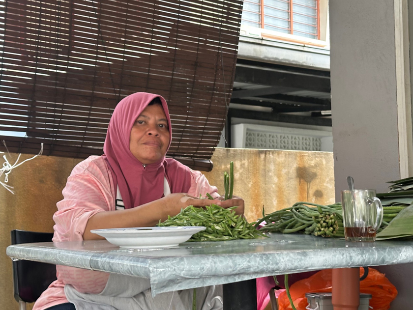 Mak Ja memotong sayur-sayuran sambil berceloteh bersama pekerja dan pelanggan warungnya. 