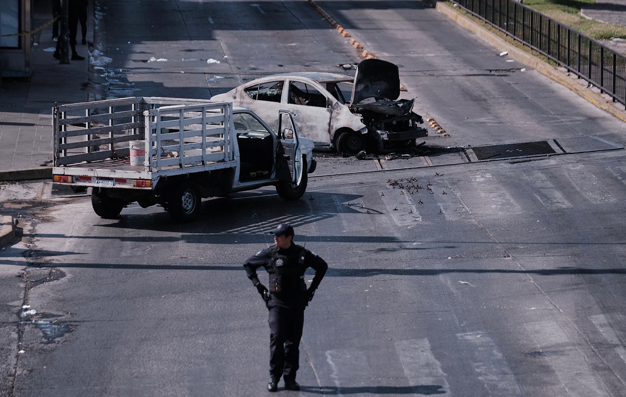 A police officer stands guard by a charred vehicle after it was set on fire, on a road in Guadalajara, Jalisco state, Mexico, Sunday, Feb. 22, 2026, after the death of the leader of the Jalisco New Generation Cartel, Nemesio Rubén Oseguera Cervantes, known as "El Mencho." (AP Photo/Alejandra Leyva)
