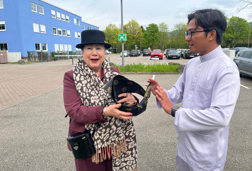 Pereka topi daripada Perancis, Marie Francophonie mendengar penjelasan daripada Ahmad Taufeq Ismadi mengenai keunikan tanjak yang dipakainya di hari graduasi di Offenburg, Jerman baru-baru ini. - Gambar Astro AWANI